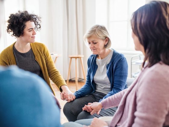 Men and women sitting in a circle during group therapy, supporting each other.